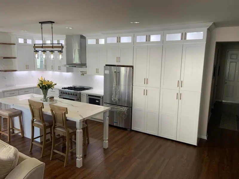 Finished kitchen with white cabinets to the ceiling, a stainless hood, an island table with stools and a wood plank floor