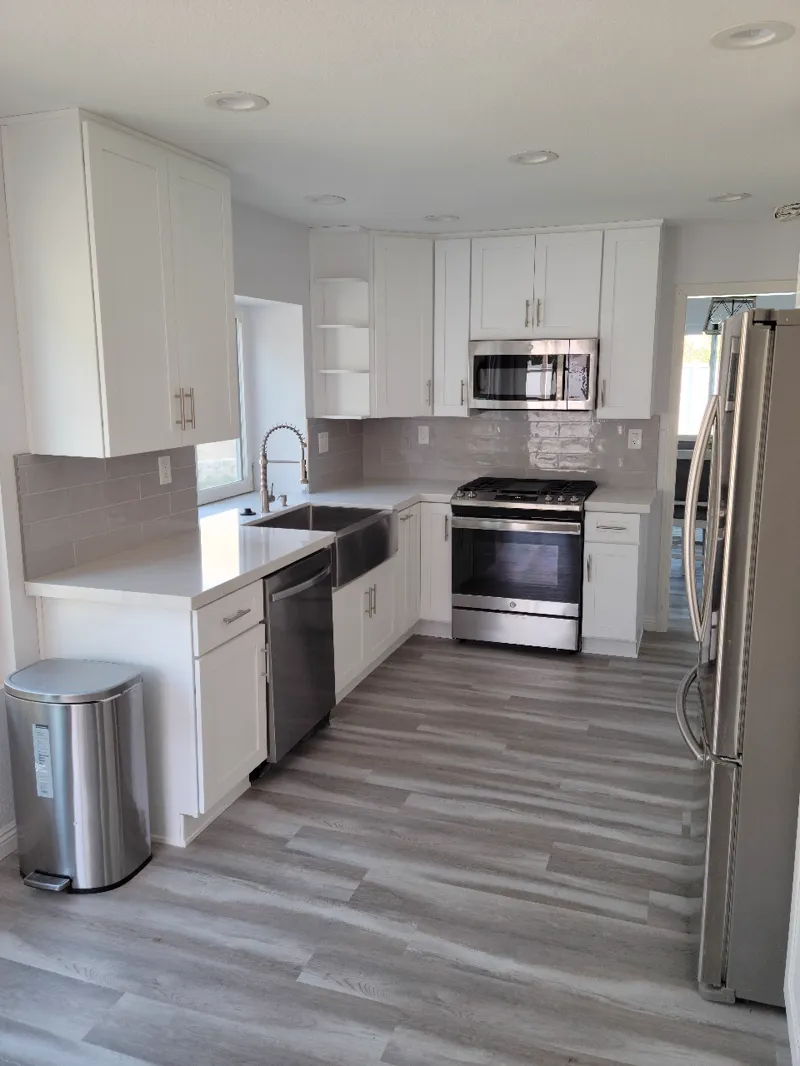 White kitchen with a farmhouse sink, gray plank floor and stainless range